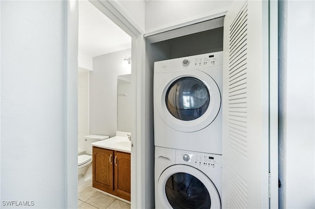 clothes washing area with light tile patterned floors, stacked washer / dryer, laundry area, and a sink