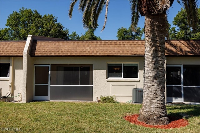 back of house featuring stucco siding, mansard roof, a yard, and a shingled roof