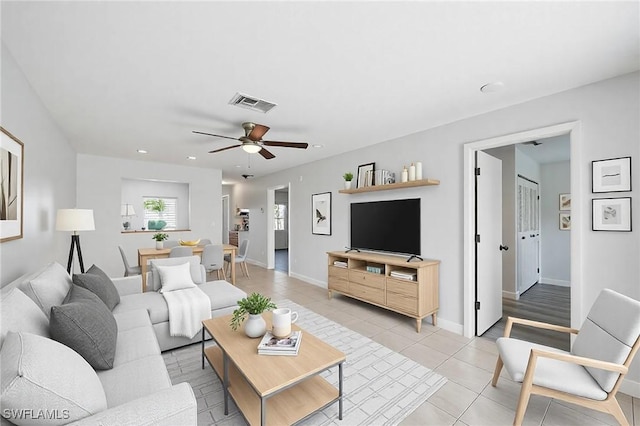 living room with light tile patterned floors, visible vents, a ceiling fan, and baseboards