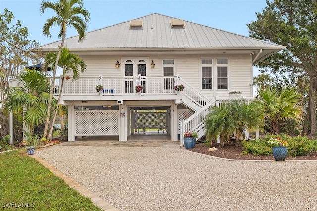 beach home featuring stairway, gravel driveway, covered porch, metal roof, and a carport