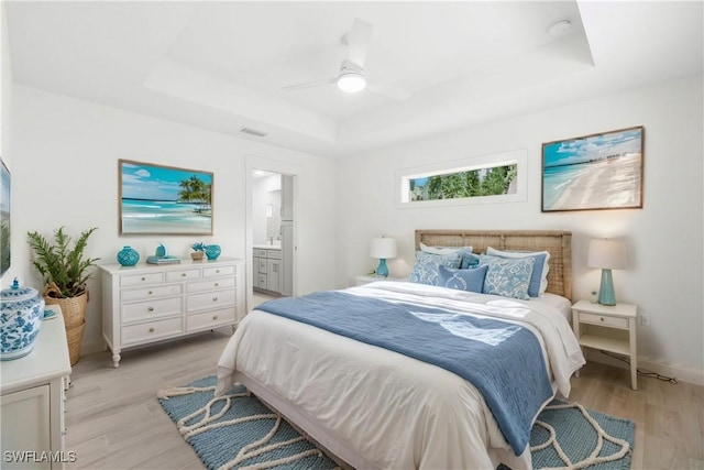 bedroom featuring visible vents, connected bathroom, a raised ceiling, and light wood-style floors