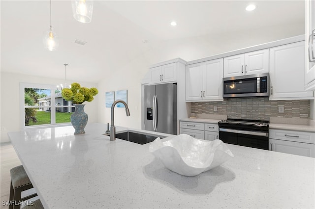 kitchen with lofted ceiling, a sink, decorative backsplash, appliances with stainless steel finishes, and decorative light fixtures