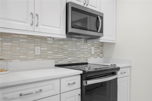 kitchen featuring stainless steel microwave, backsplash, range with electric stovetop, white cabinetry, and light stone countertops