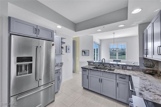 kitchen featuring light stone counters, a peninsula, gray cabinets, a sink, and stainless steel appliances