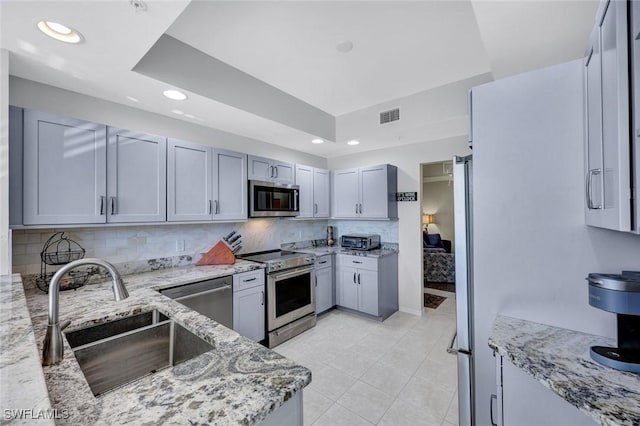 kitchen featuring light stone countertops, visible vents, a sink, stainless steel appliances, and backsplash