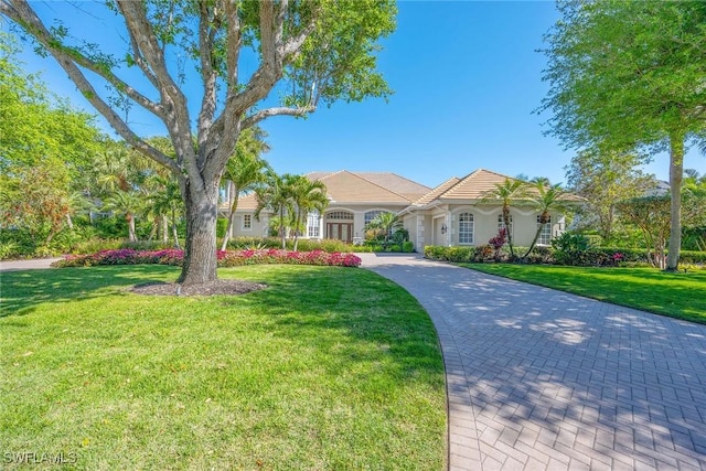 mediterranean / spanish home featuring stucco siding, driveway, a front lawn, and a tiled roof