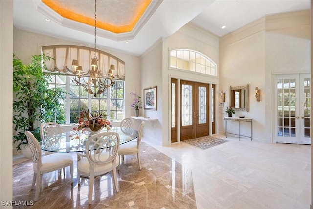 foyer entrance with a notable chandelier, marble finish floor, ornamental molding, a tray ceiling, and french doors