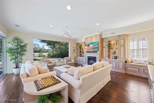 living room with visible vents, dark wood-style flooring, ceiling fan, ornamental molding, and a lit fireplace