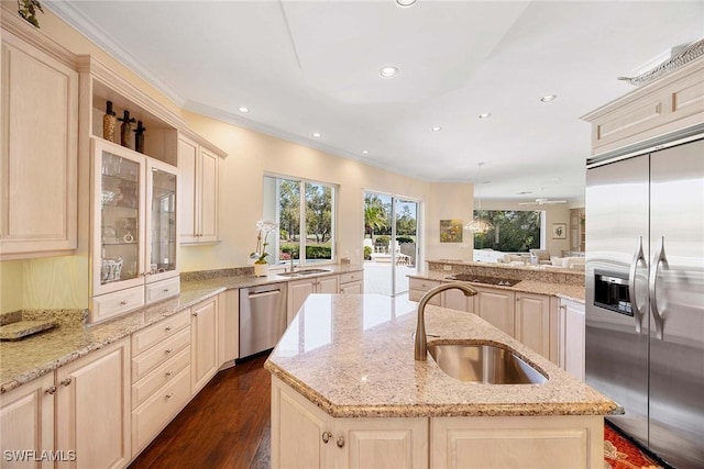 kitchen with an island with sink, a sink, stainless steel appliances, dark wood-type flooring, and cream cabinets