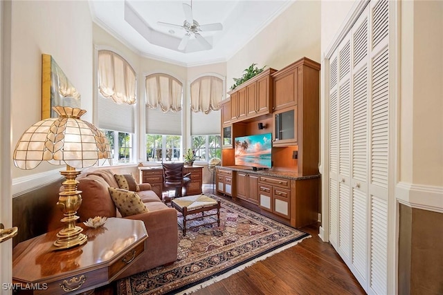 living area with a tray ceiling, dark wood-style floors, a ceiling fan, and ornamental molding