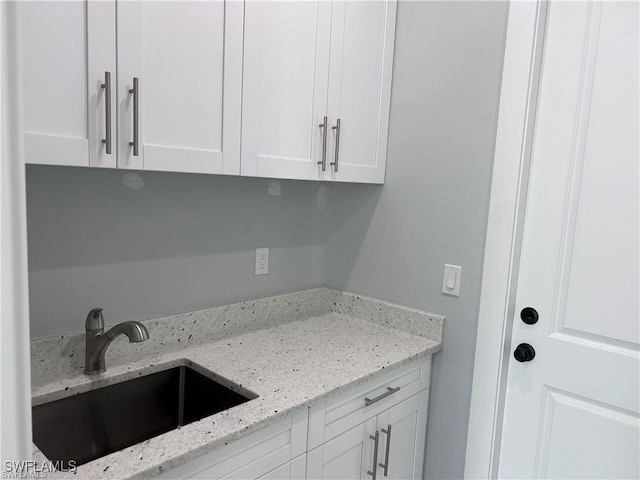 kitchen with a sink, light stone counters, and white cabinetry