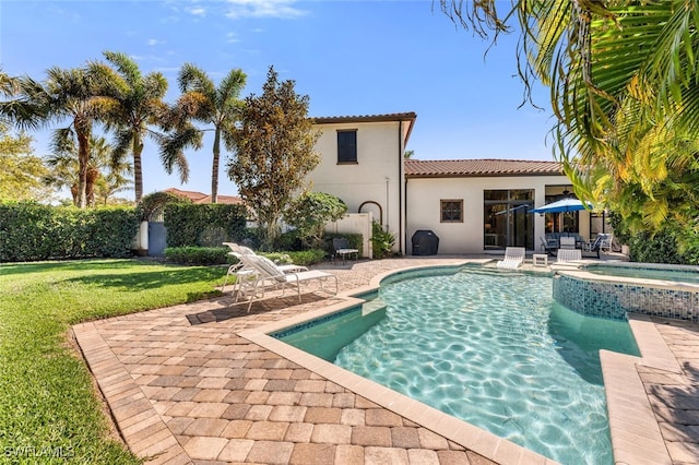 back of house featuring a pool with connected hot tub, a tile roof, stucco siding, a yard, and a patio