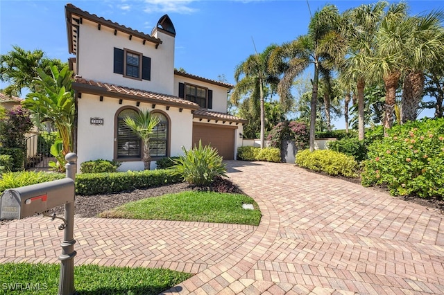 mediterranean / spanish home with stucco siding, an attached garage, a tile roof, and decorative driveway