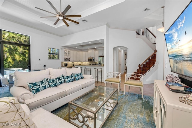 living room featuring visible vents, arched walkways, a raised ceiling, ceiling fan, and stairs