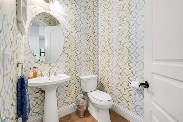 bathroom with baseboards, wallpapered walls, a sink, tile patterned flooring, and toilet