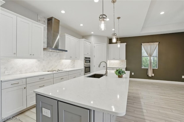 kitchen featuring a center island with sink, a sink, decorative backsplash, appliances with stainless steel finishes, and wall chimney exhaust hood