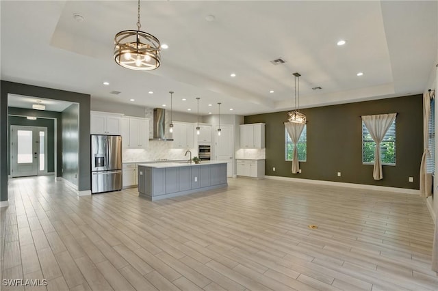 kitchen featuring a sink, a raised ceiling, appliances with stainless steel finishes, and wall chimney range hood