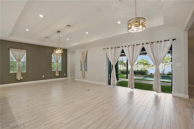 empty room featuring visible vents, an inviting chandelier, light wood-type flooring, and a tray ceiling