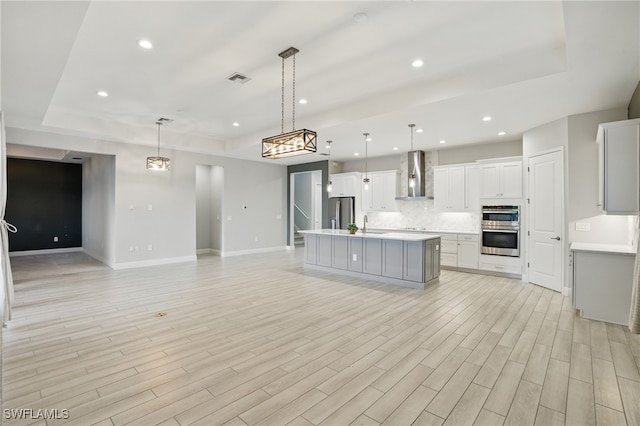 kitchen featuring open floor plan, appliances with stainless steel finishes, a raised ceiling, and wall chimney exhaust hood