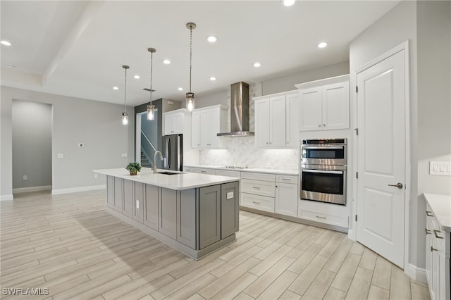 kitchen featuring tasteful backsplash, wall chimney range hood, a center island with sink, light countertops, and stainless steel appliances