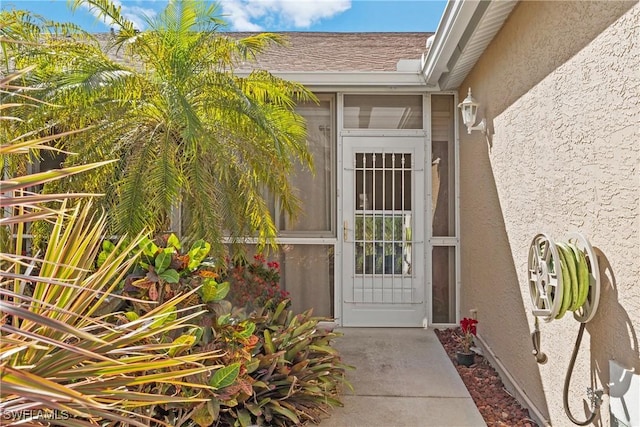 entrance to property with stucco siding and roof with shingles