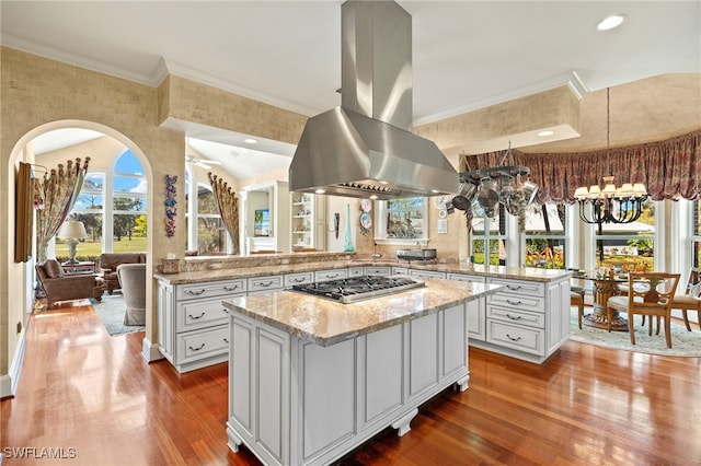 kitchen featuring a kitchen island, stainless steel gas cooktop, a peninsula, island exhaust hood, and a notable chandelier