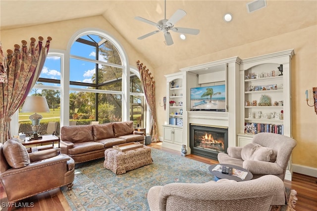 living area featuring visible vents, high vaulted ceiling, a ceiling fan, a glass covered fireplace, and wood finished floors