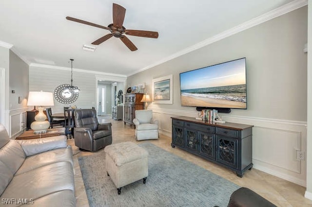 living room with wainscoting, ornamental molding, a ceiling fan, and a decorative wall