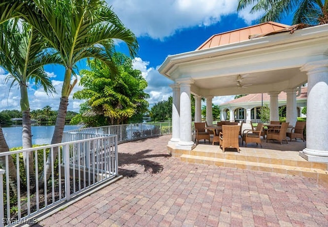 view of patio with ceiling fan, a water view, fence, a gazebo, and outdoor dining area