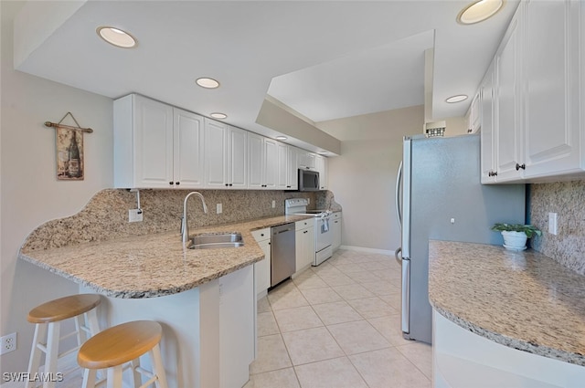 kitchen with a breakfast bar, a peninsula, stainless steel appliances, white cabinetry, and a sink