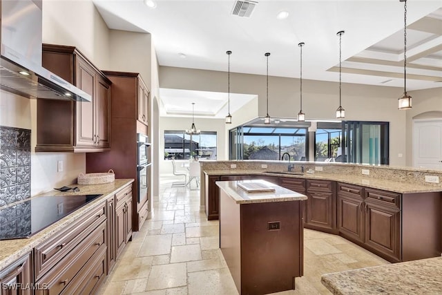 kitchen featuring a large island, a sink, stone tile floors, wall chimney range hood, and a raised ceiling