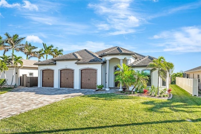 mediterranean / spanish home with decorative driveway, fence, a front yard, a garage, and a tiled roof