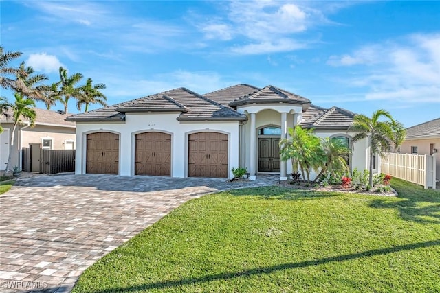 view of front of property with a front lawn, fence, a tile roof, decorative driveway, and a garage