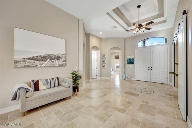 entrance foyer featuring a tray ceiling, stone tile floors, a barn door, arched walkways, and baseboards