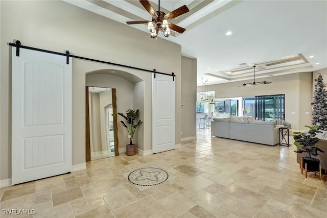 living room featuring a barn door, ceiling fan with notable chandelier, a tray ceiling, and stone tile flooring