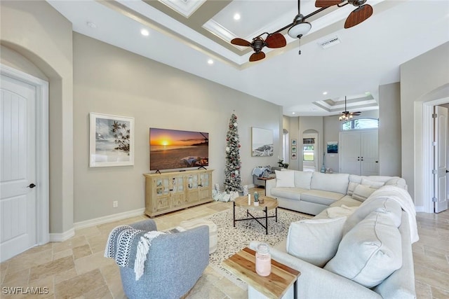 living area featuring a ceiling fan, visible vents, baseboards, arched walkways, and a raised ceiling