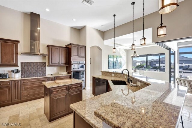 kitchen with visible vents, wall chimney range hood, a large island with sink, stainless steel appliances, and a sink