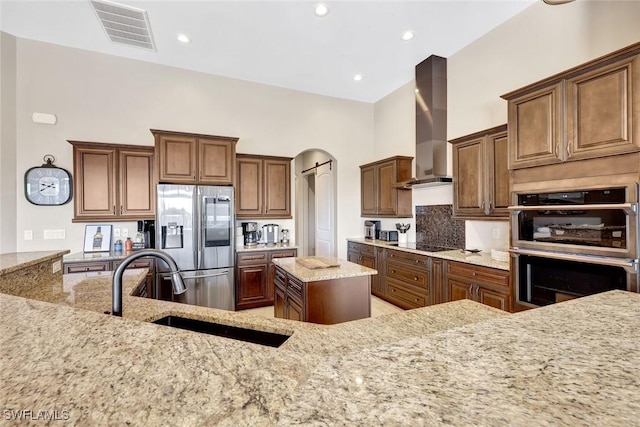 kitchen with visible vents, wall chimney range hood, light stone counters, appliances with stainless steel finishes, and a sink