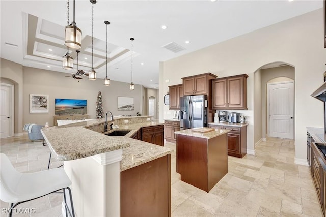 kitchen featuring visible vents, a sink, stainless steel fridge, arched walkways, and a large island with sink