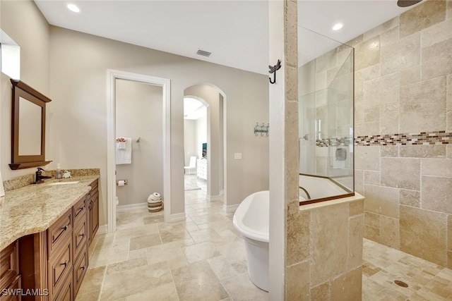 full bathroom featuring a freestanding tub, stone tile flooring, baseboards, walk in shower, and vanity