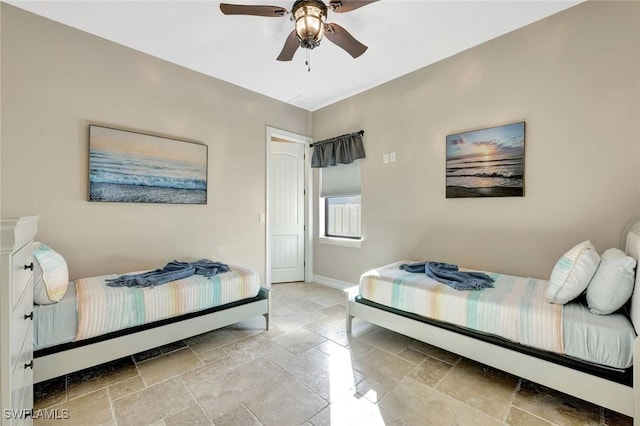 bedroom with stone tile floors, ceiling fan, and baseboards