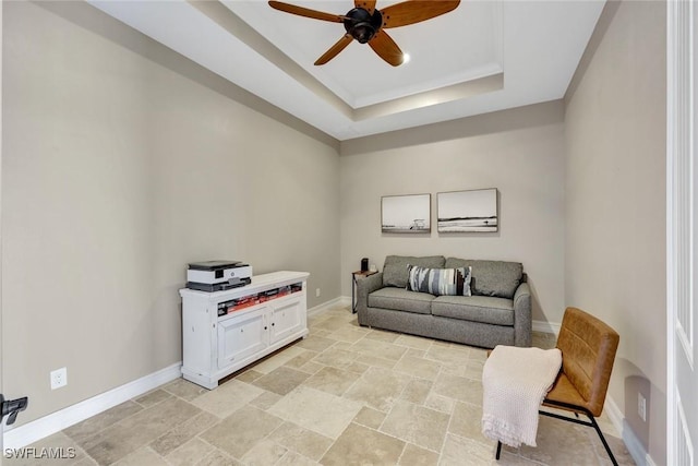 sitting room featuring a tray ceiling, a ceiling fan, baseboards, and stone finish flooring