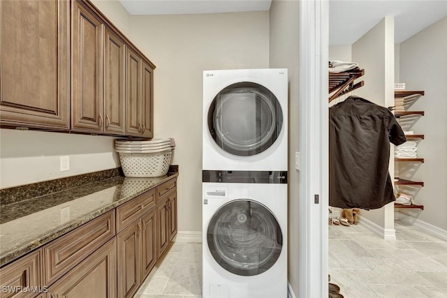 washroom with cabinet space, baseboards, and stacked washing maching and dryer