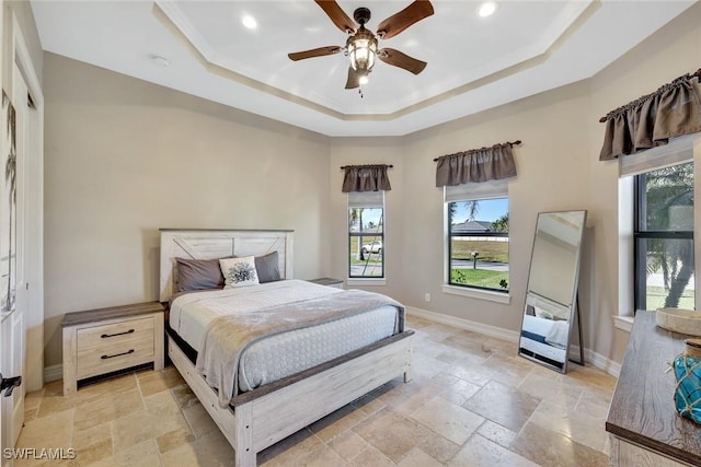 bedroom with baseboards, a raised ceiling, multiple windows, and stone tile flooring