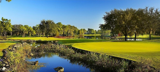 view of home's community with view of golf course, view of scattered trees, a lawn, and a water view