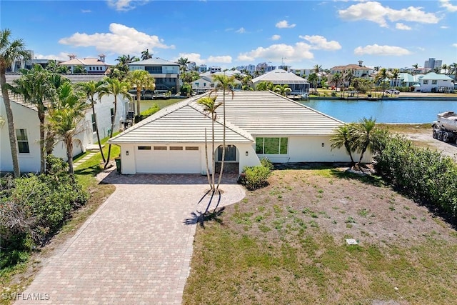 ranch-style house with decorative driveway, an attached garage, a residential view, and a water view