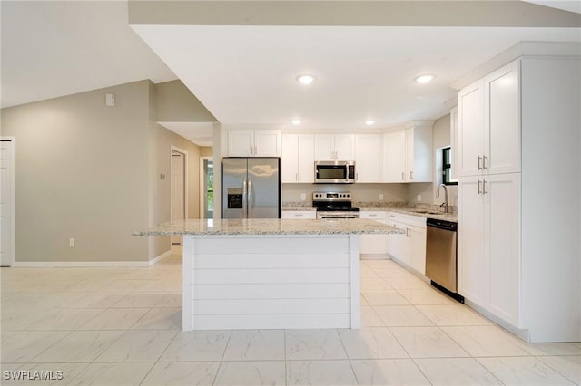 kitchen featuring light stone countertops, a kitchen island, a sink, stainless steel appliances, and white cabinets