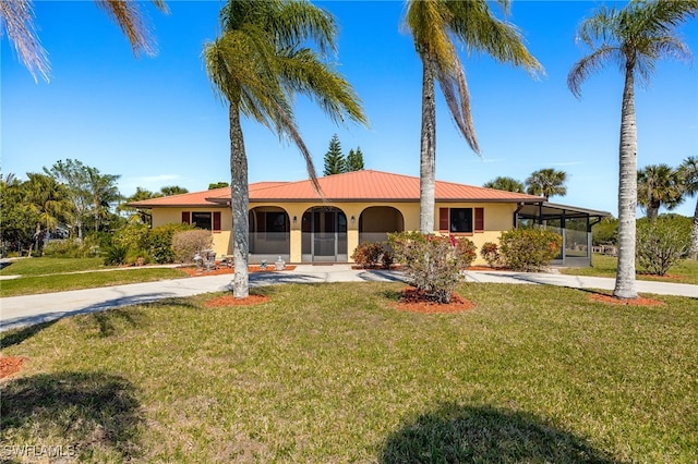 view of front facade with stucco siding, metal roof, a front yard, and a sunroom