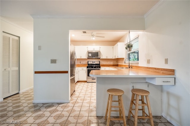 kitchen featuring a peninsula, a sink, decorative backsplash, appliances with stainless steel finishes, and crown molding