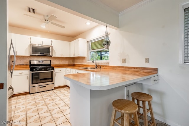 kitchen with a peninsula, a sink, appliances with stainless steel finishes, crown molding, and backsplash